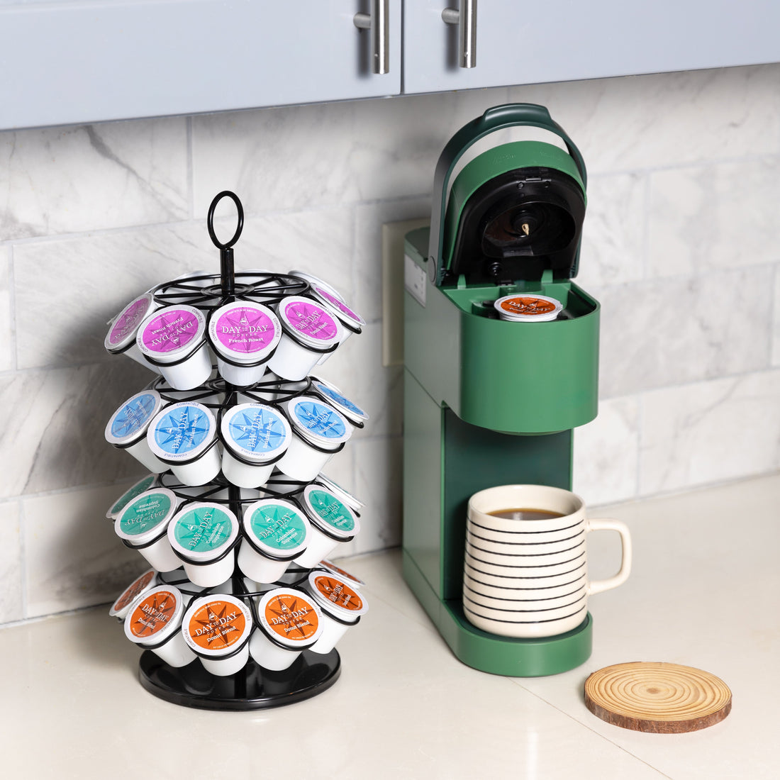 Coffee station featuring a green single-serve coffee maker brewing into a striped ceramic mug, with a rotating pod holder filled with colorful Day to Day Coffee K-Cups in various flavors