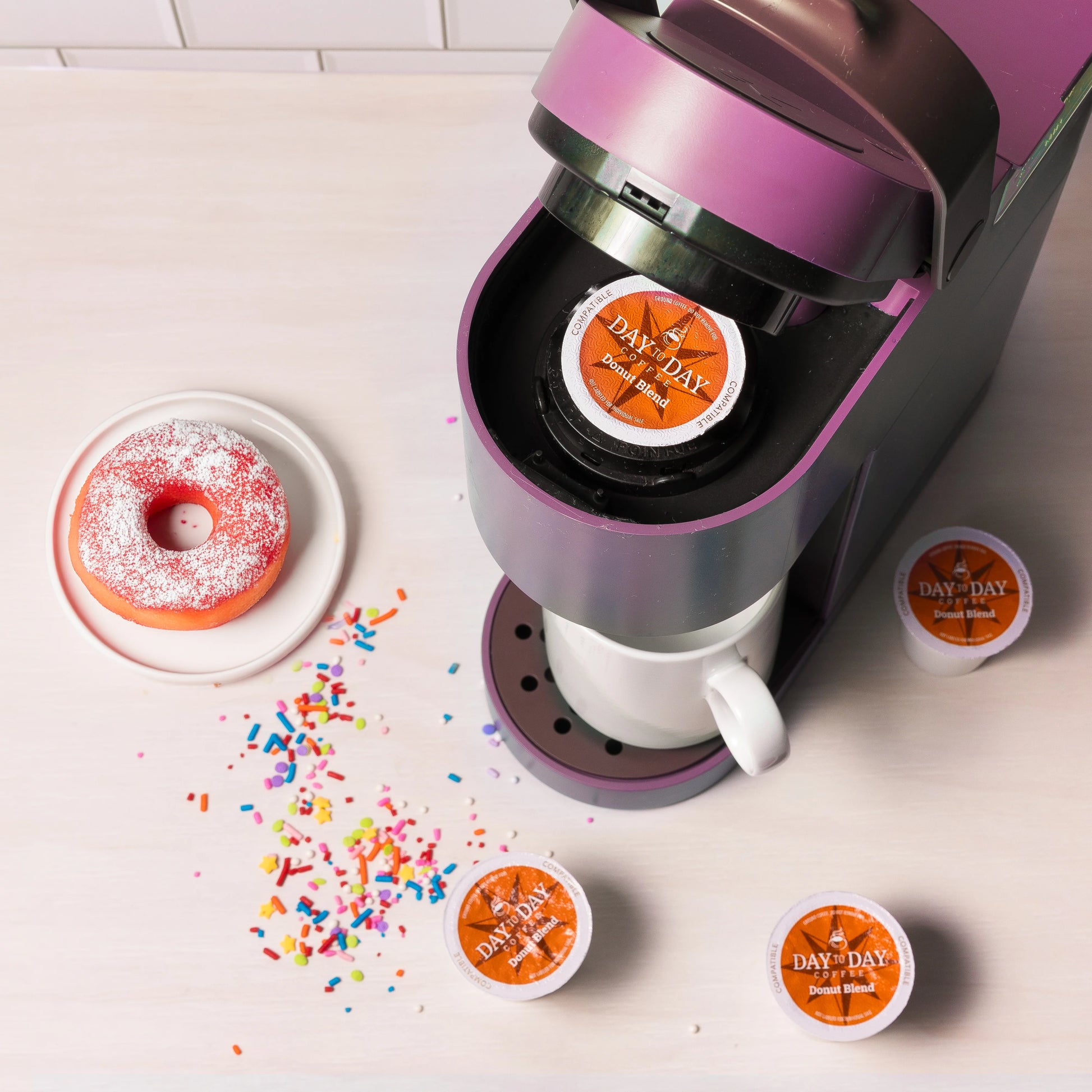Donut Blend coffee pod from Day to Day Coffee placed in Keurig machine with sprinkled donut beside – medium roast